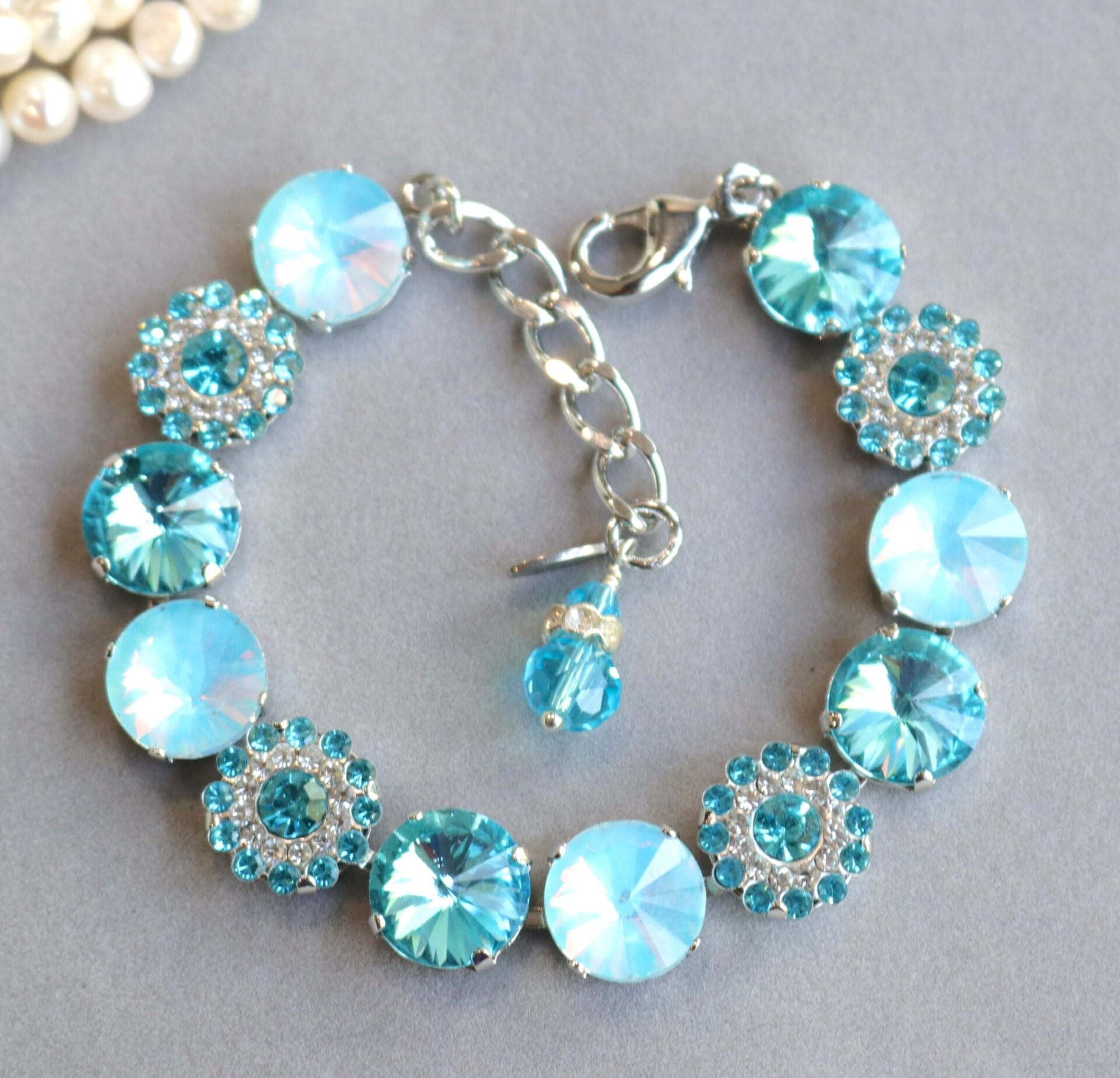 Shimmer in elegance with the Aqua Blossom Bracelet, featuring aqua crystals and rhinestone blossoms. Adjustable silver design for bridal, prom, or evening wear.